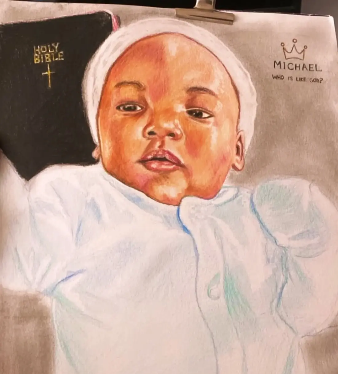 Coloured-pencil portrait of a baby in a white outfit beside a Bible.