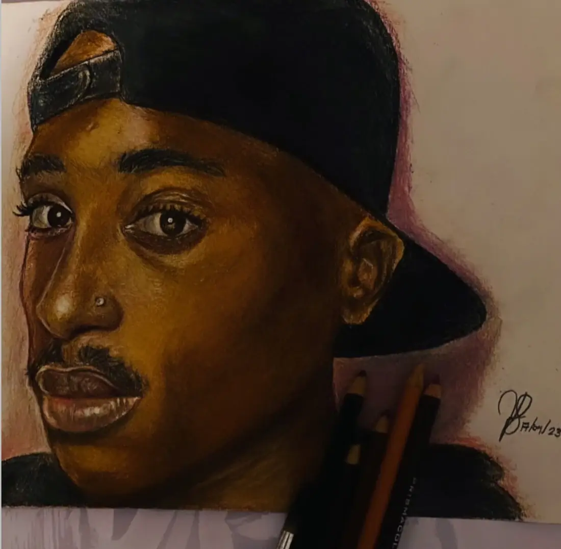 Coloured-pencil portrait study featuring a backwards cap, with pencils beside the drawing.