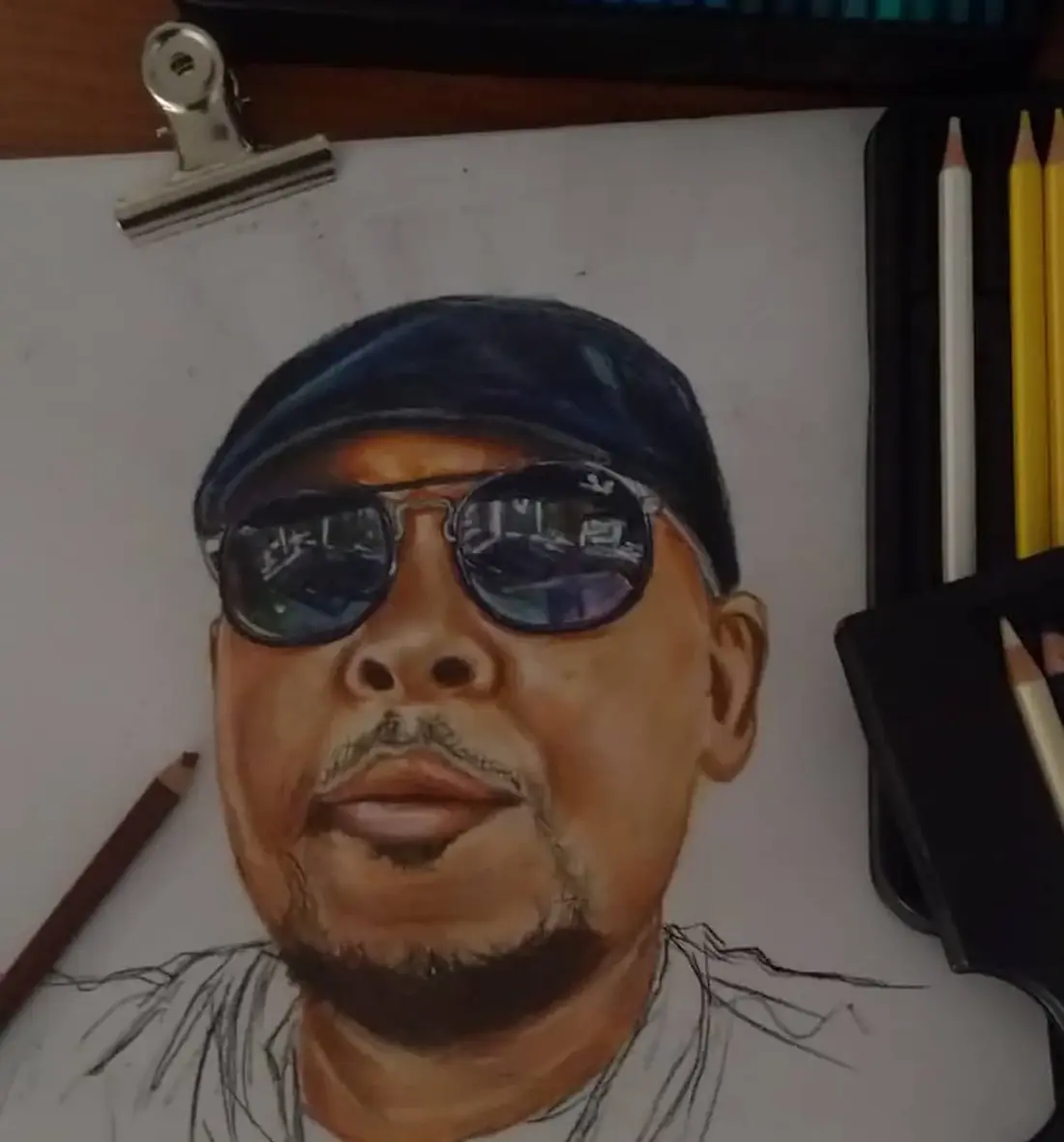 A coloured-pencil portrait in progress, showing a cap and reflective sunglasses.