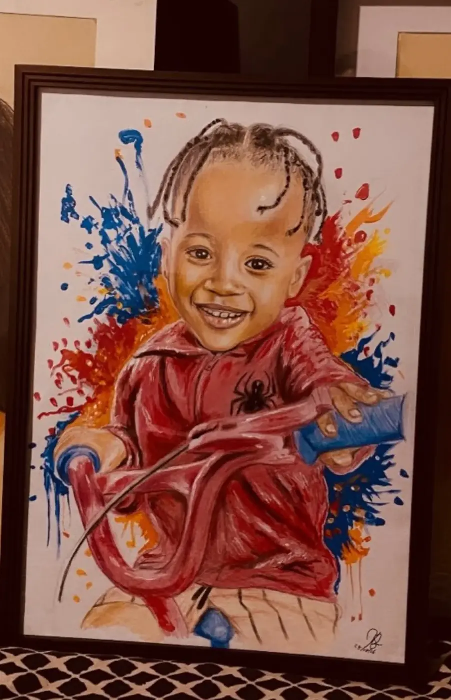 Framed portrait of a smiling child in red, surrounded by vivid colour splashes.